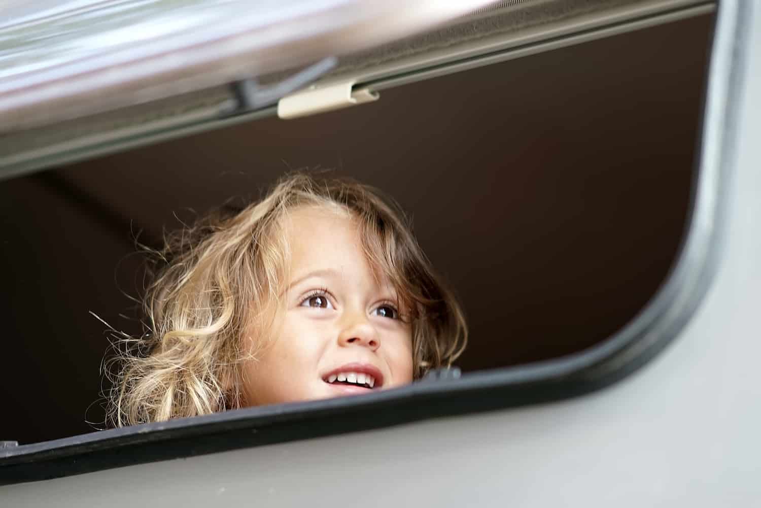 the little girl looks out happy of the camper window